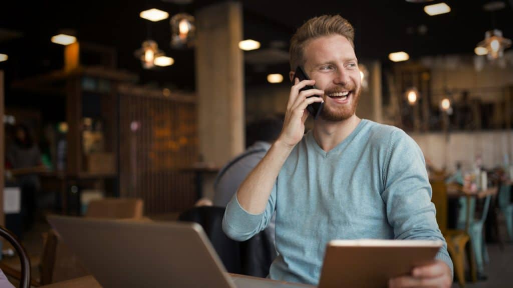 A smiling man at a cafe talking on the phone.