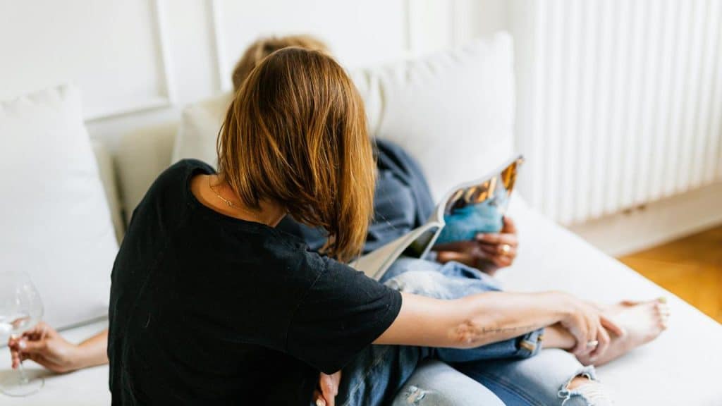 A couple sitting on a couch reading a magazine together.