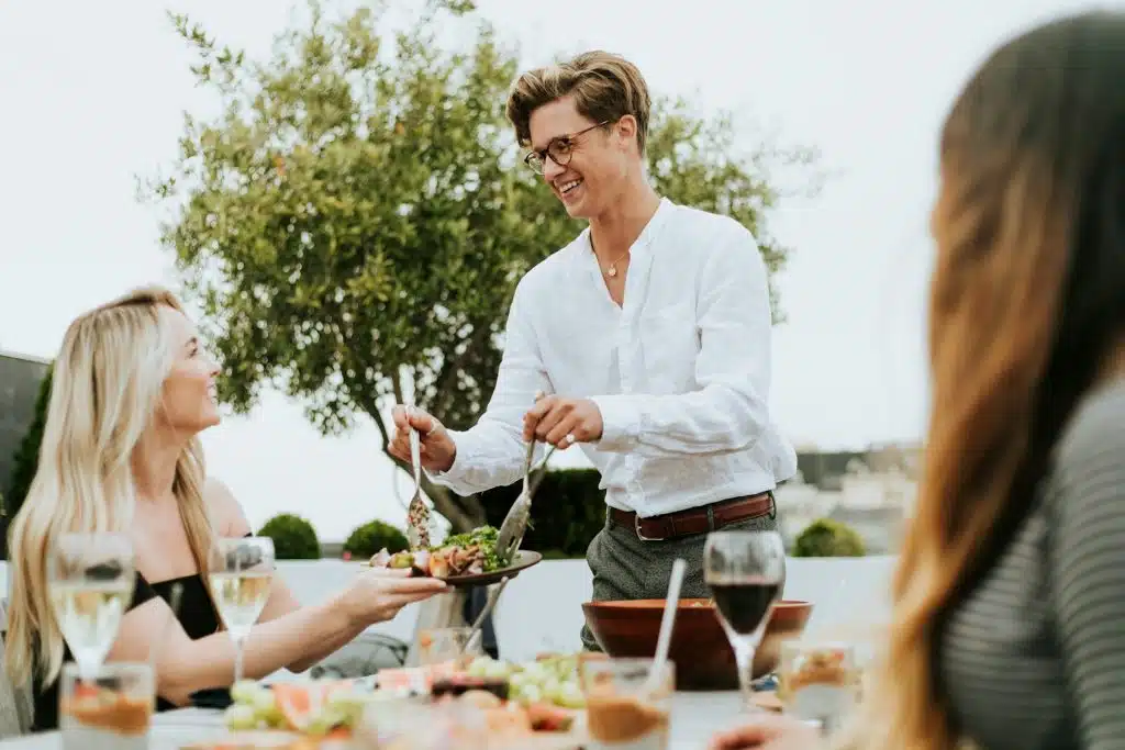 The man is serving salad at a rooftop party.