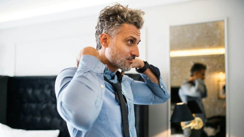 A stylish middle-aged man is adjusting his tie in front of a mirror.
