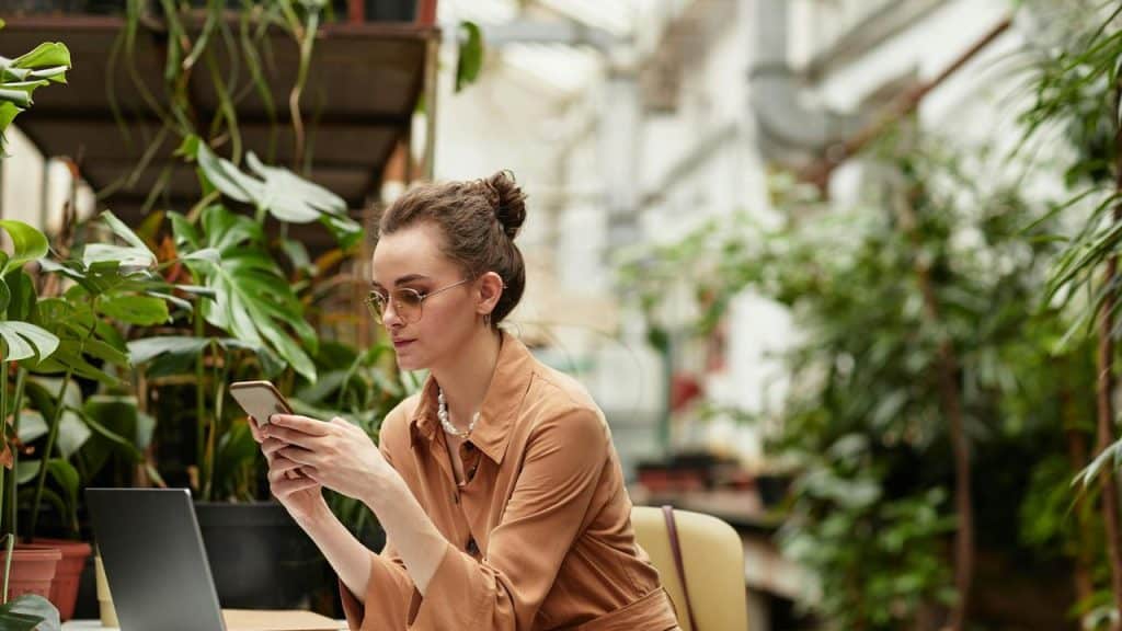 A woman sitting at a table surrounded by plants while looking at her phone.