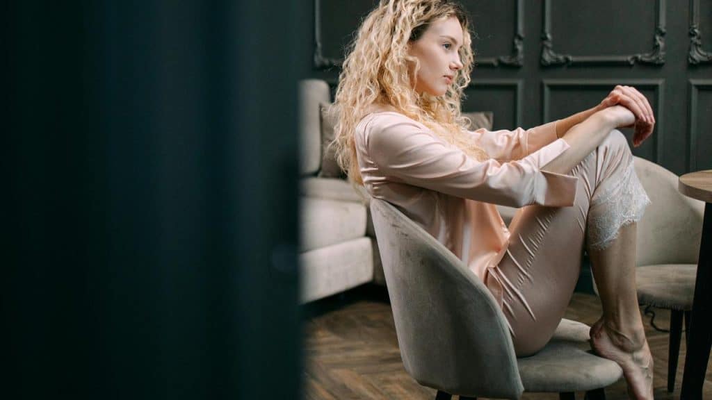A woman sitting on a chair with her knees drawn up, looking thoughtful.
