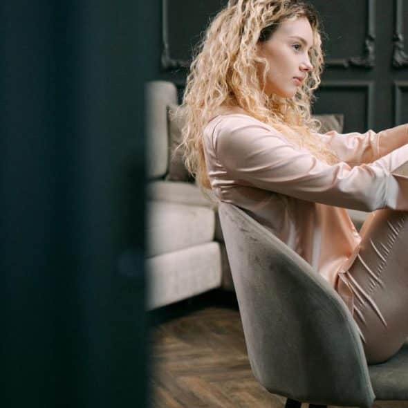 A woman sitting on a chair with her knees drawn up, looking thoughtful.