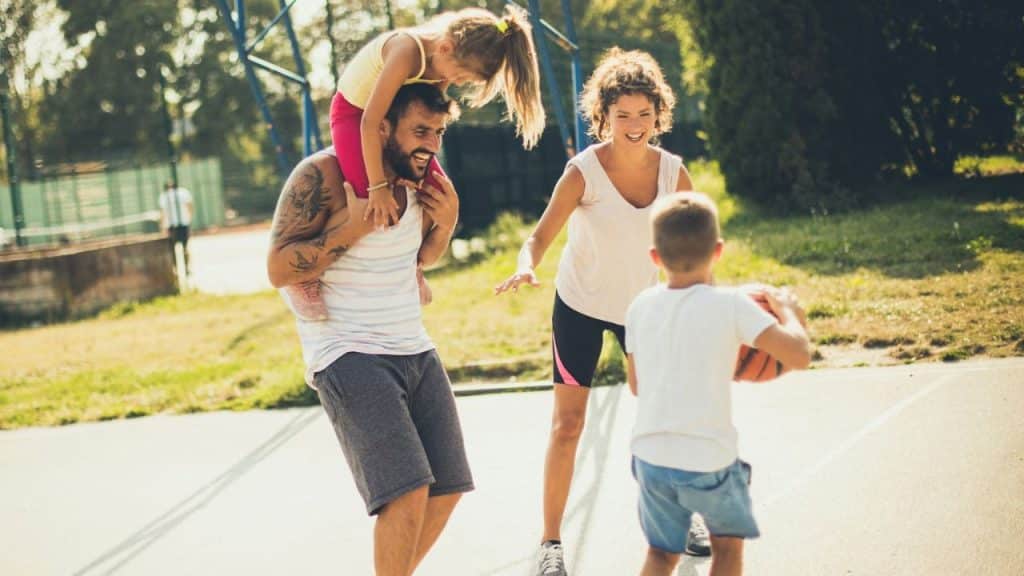 Family of four playing outdoors on a basketball court in bright sunlight.