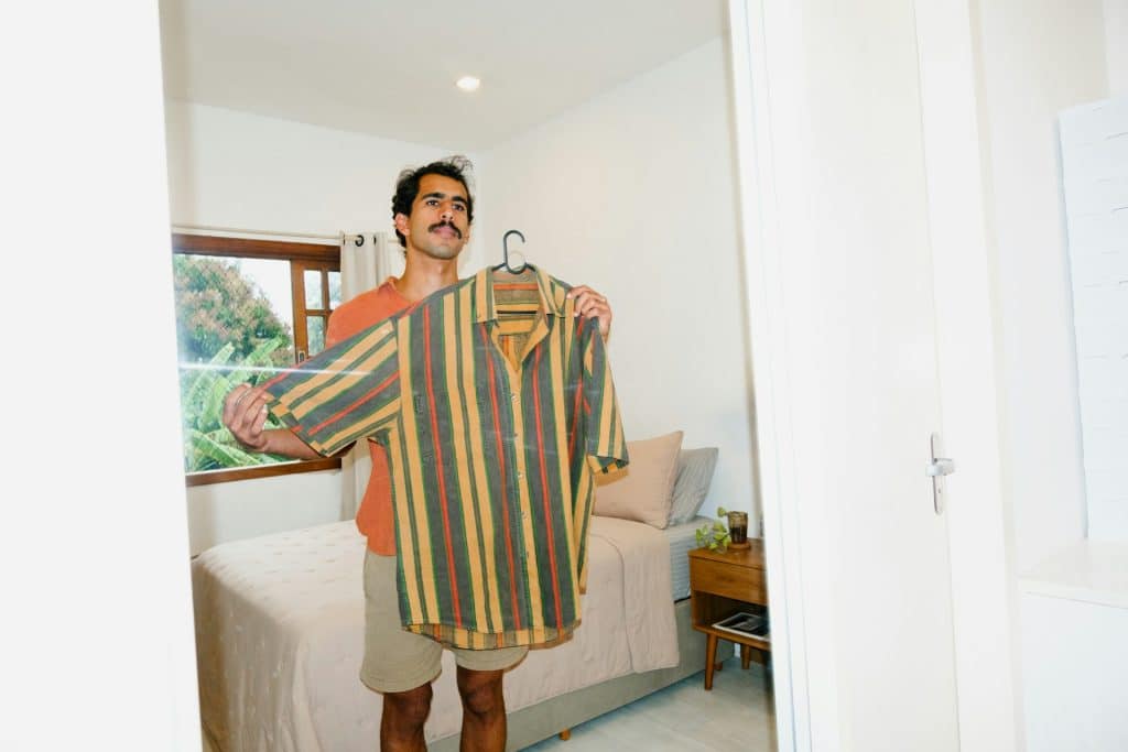 The man holds up the shirt while looking at the mirror.