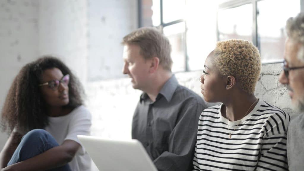 A group of people sitting together and talking with a laptop.