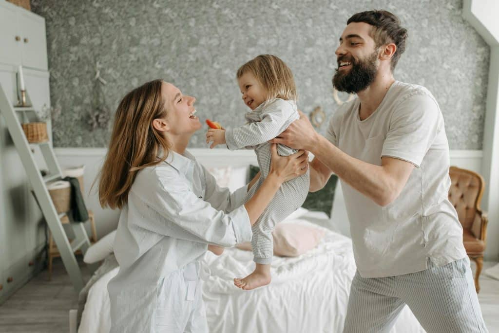 The parents are playing with their daughter in the bedroom.