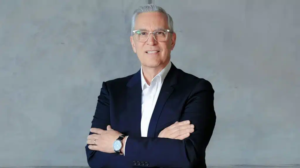 Middle-aged man in a dark suit and glasses with arms crossed.
