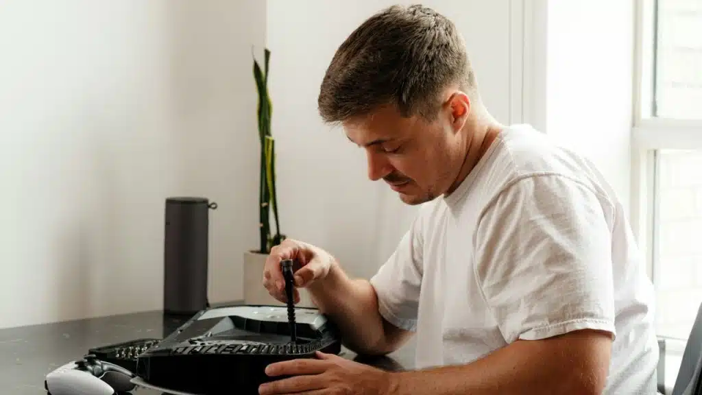 Man in a white t-shirt using a screwdriver to fix an electronic device.