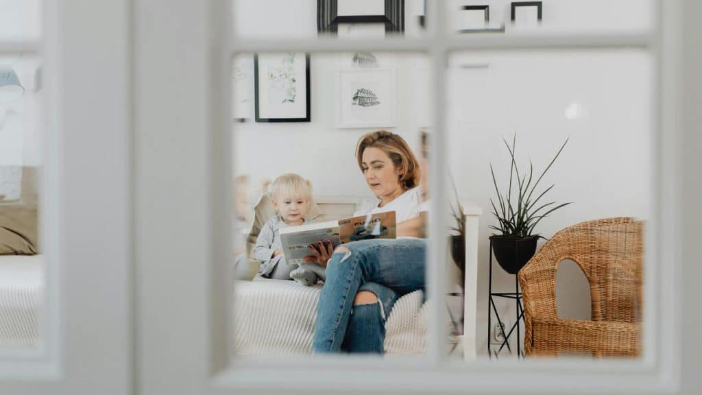 A woman reading a book to a young child in a cozy living room.