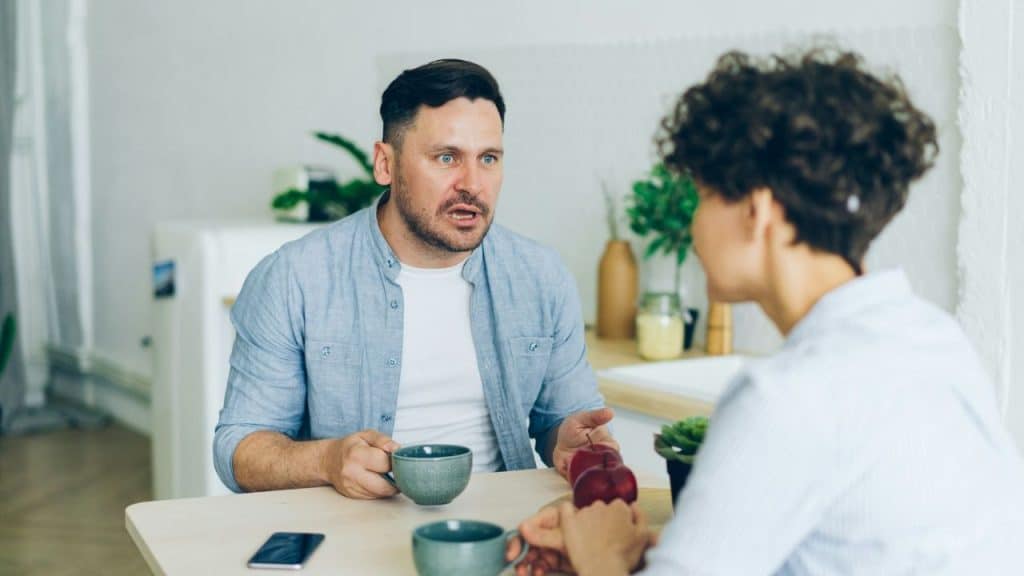 Man with wide eyes and open mouth talking to a person across a table.