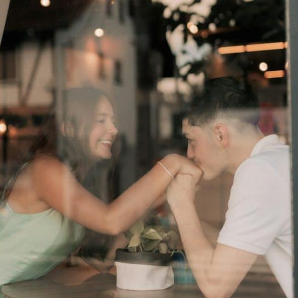 A couple smiling and holding hands across a table in a cozy café.