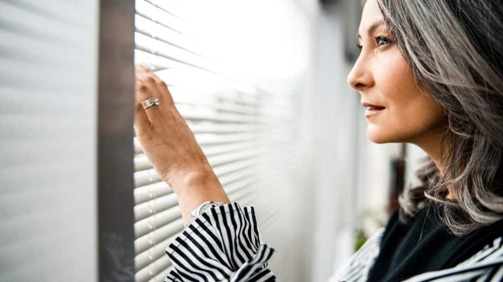 A woman looking outside through window blinds.