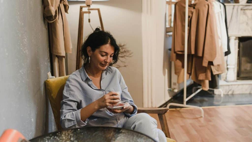 A person sitting in a cozy room, smiling while holding a cup.