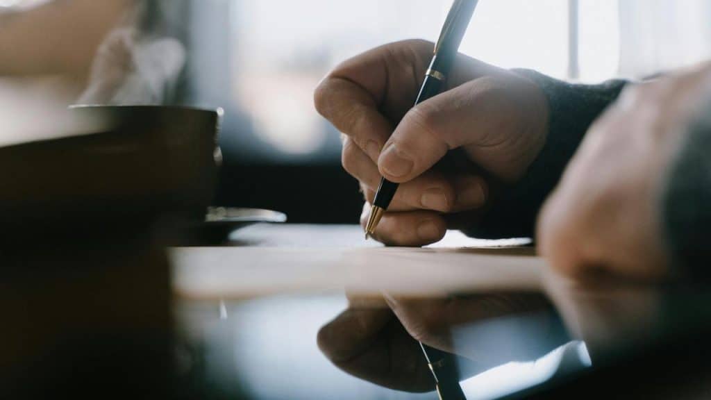 A person writing with a pen on paper at a desk.