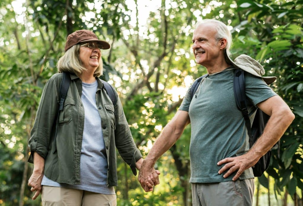 The elderly couple is holding hands while walking in the forest.