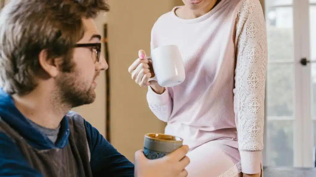A man and a woman having a conversation while holding coffee mugs.