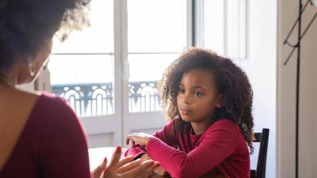 A young girl sitting at a table listening to an adult.