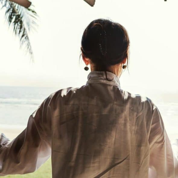 A woman standing by open doors looking out at the beach.