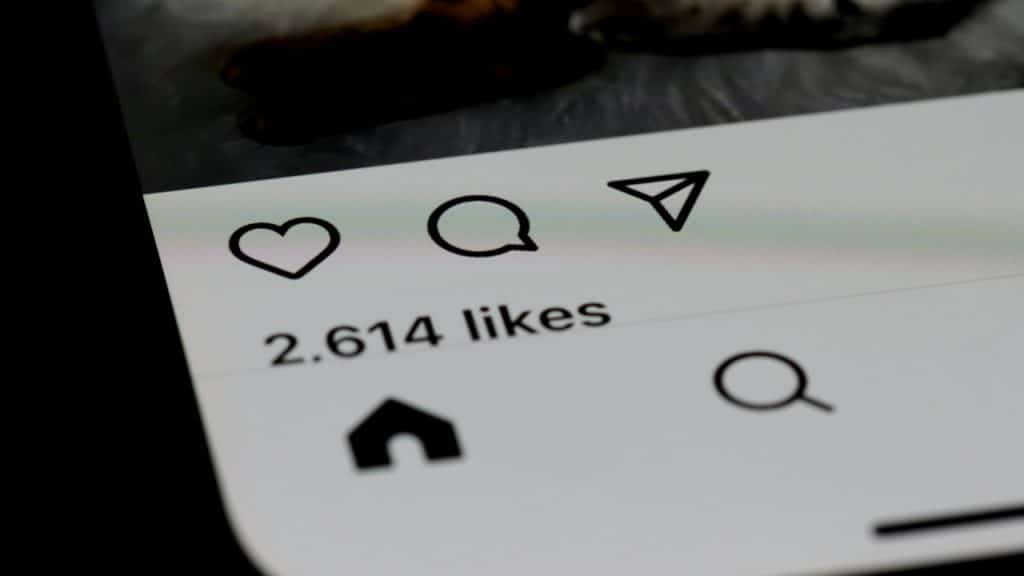 Close-up of a smartphone screen showing 2,614 likes and icons for like, comment, and share beneath an Instagram post.