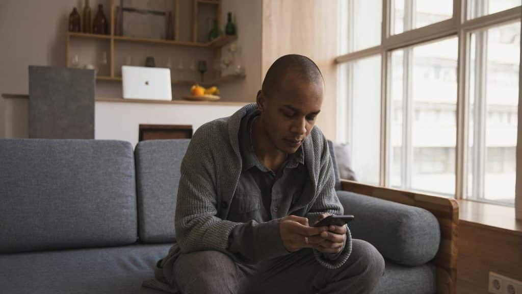 A man sitting on a couch looking down at his phone.