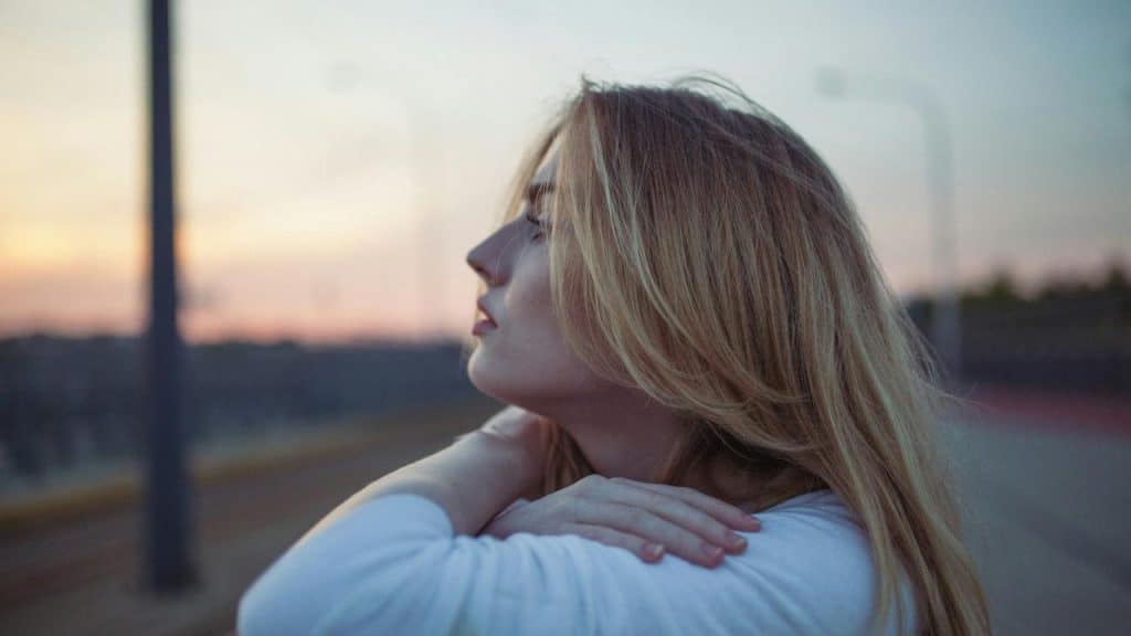 A woman resting her arms on her knees and looking into the distance at sunset.