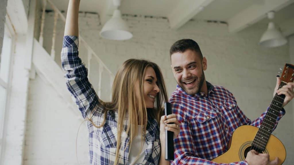 A couple singing and playing guitar together while smiling.