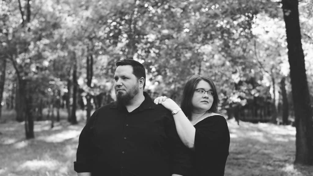 A man and woman standing in a forest.