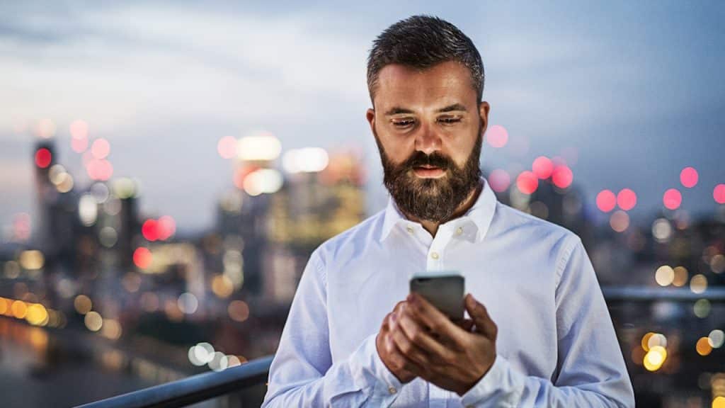 A man using his phone with a view of the urban skyline in the background.
