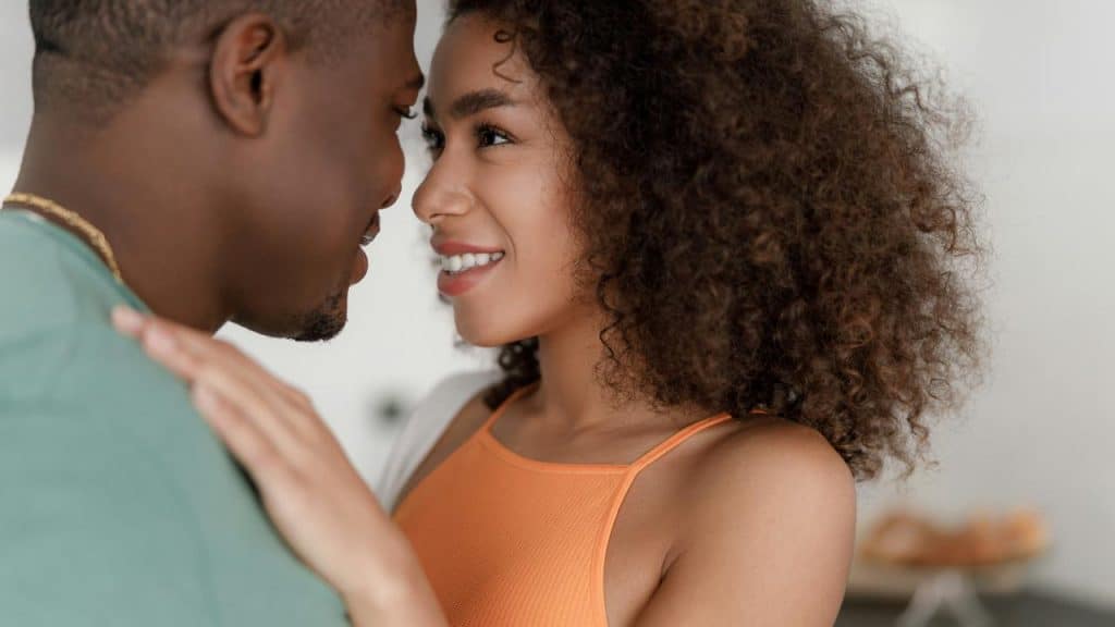 A couple standing close together, smiling and looking into each other's eyes.