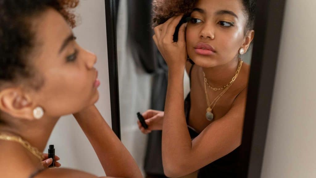 A woman applying mascara while looking in a mirror.
