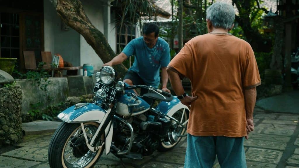 Two men are looking at a vintage, blue and white motorcycle outdoors.