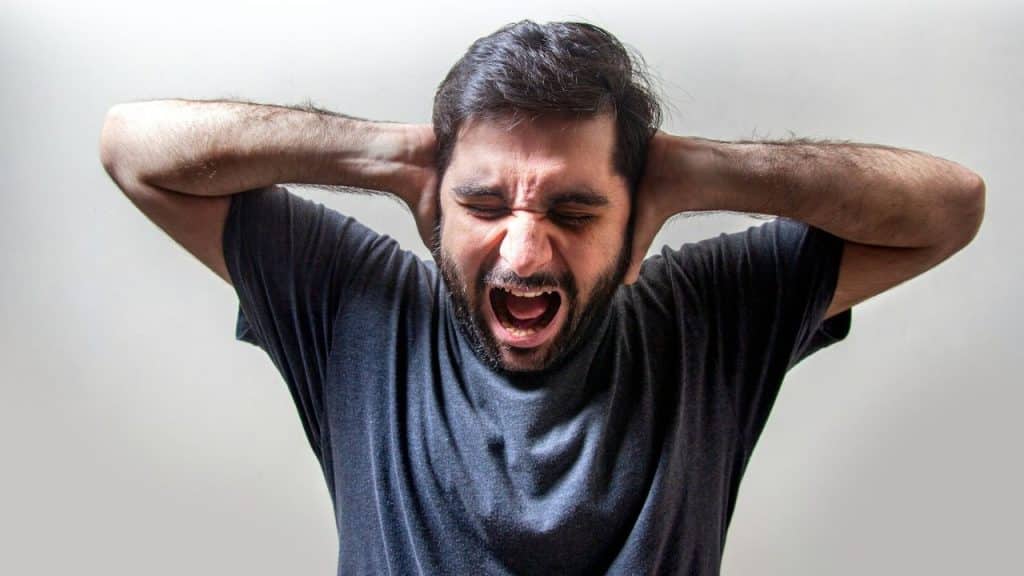A man is shouting with his eyes closed and his hands covering his ears.