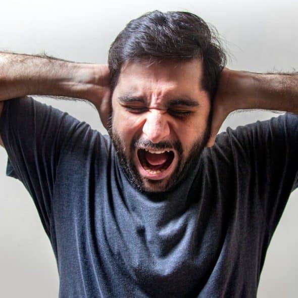 A man is shouting with his eyes closed and his hands covering his ears.