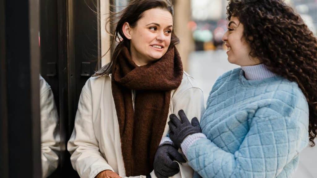 A pair of women standing outside and smiling while talking to each other.