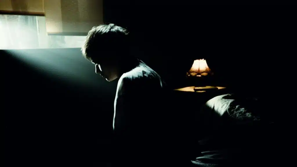Silhouetted person sits in a dark room with dramatic light falling on their profile.