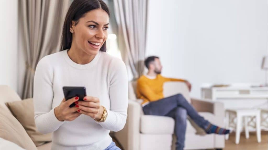 Man sitting on a couch looking distant while his partner scrolls her phone