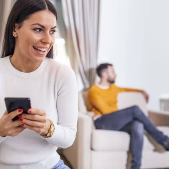 Man sitting on a couch looking distant while his partner scrolls her phone