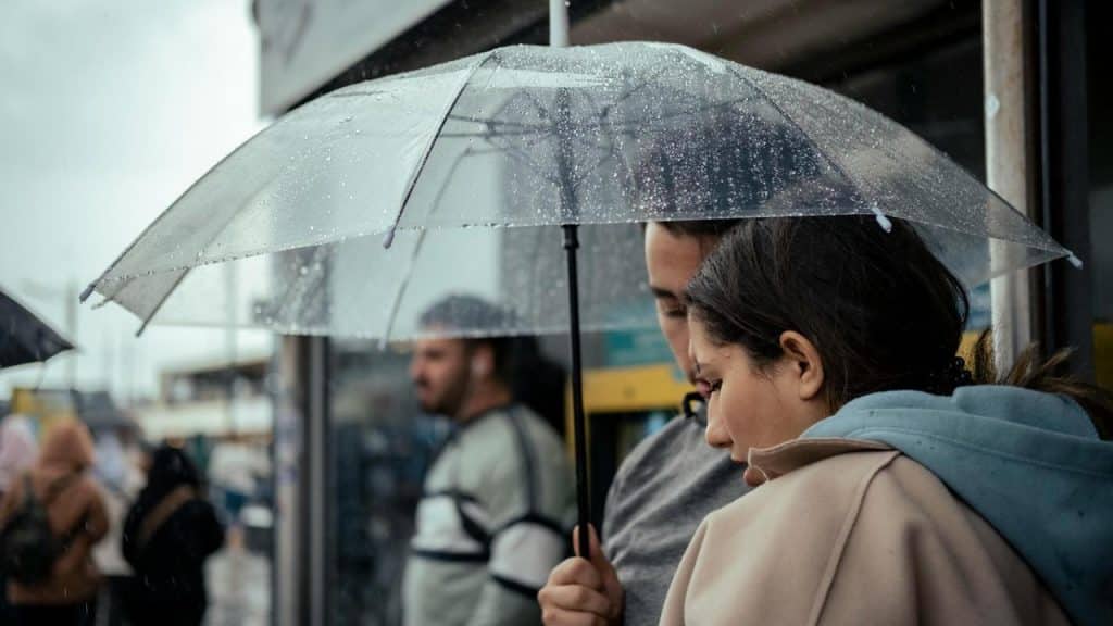 A couple standing close under a transparent umbrella on a rainy day.