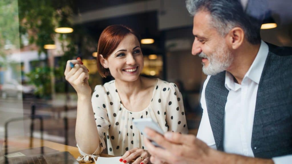 Woman smiling at man looking at a smartphone in a casual indoor setting.