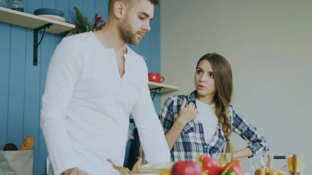 A man in a white shirt stands next to a woman in a plaid shirt who is speaking to him.