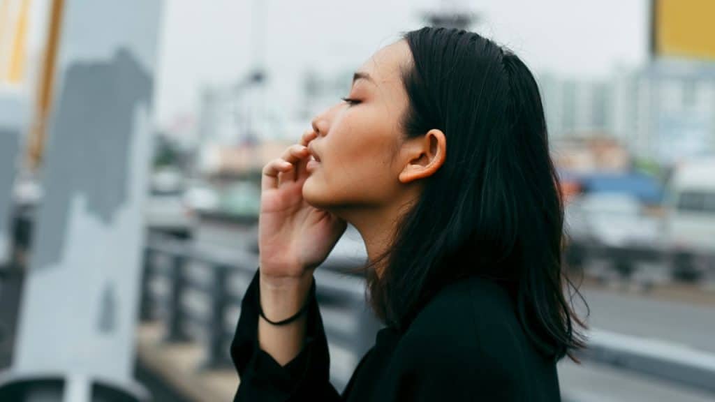 A woman with closed eyes touching her face.