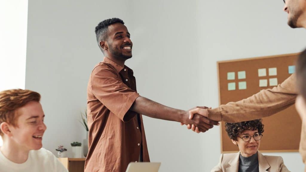 A man standing and shaking hands with another person in a meeting room.