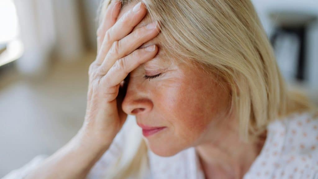 Close-up of a middle-aged woman with blonde hair holding her hand to her forehead.