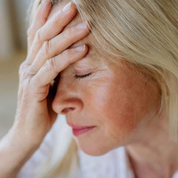 Close-up of a middle-aged woman with blonde hair holding her hand to her forehead.