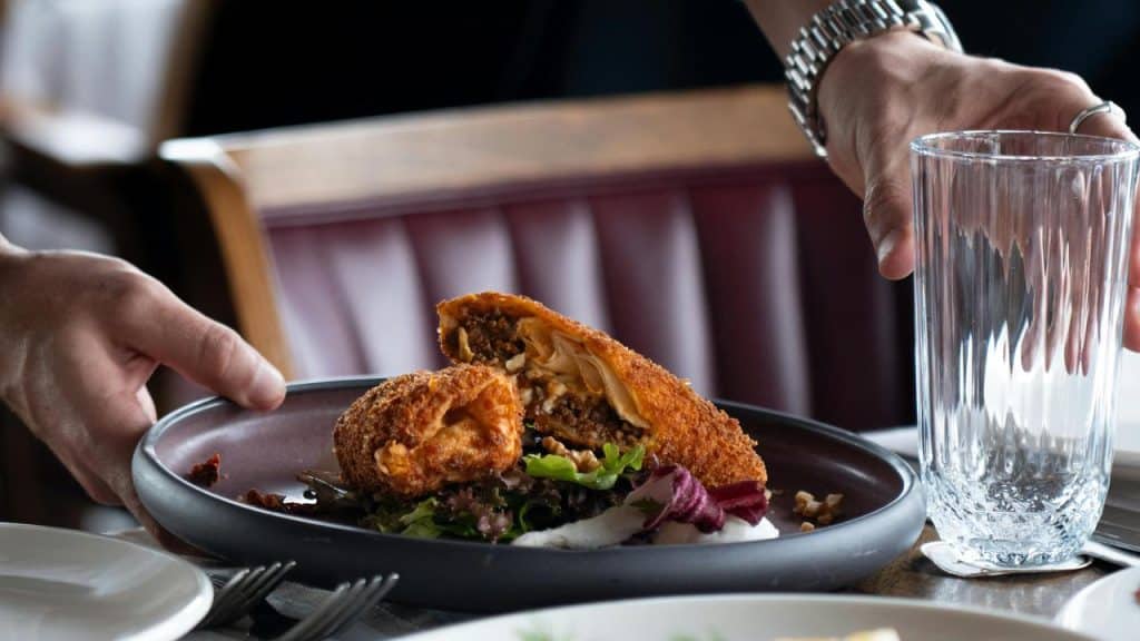 A person serving a plate of fried food with salad at a restaurant table.