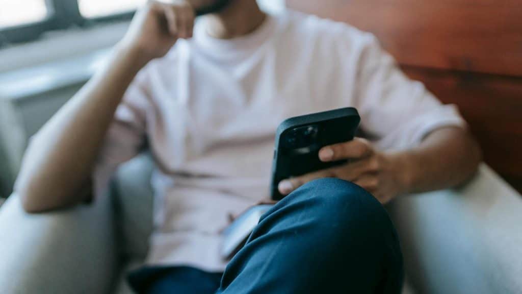 A man sitting in a chair holding a smartphone and thinking.
