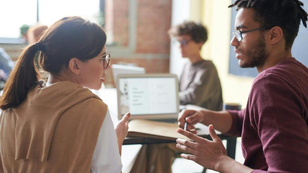 A man and woman having a discussion in an office setting with laptops on the table.