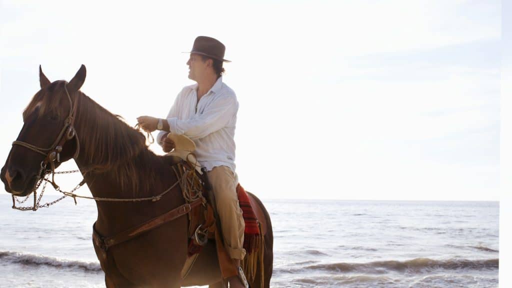 A man riding a horse on the beach.