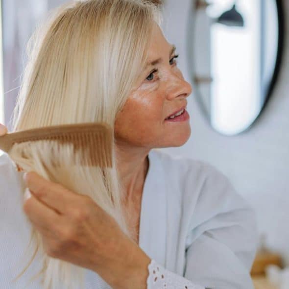 A woman combing her long blonde hair in front of a mirror.